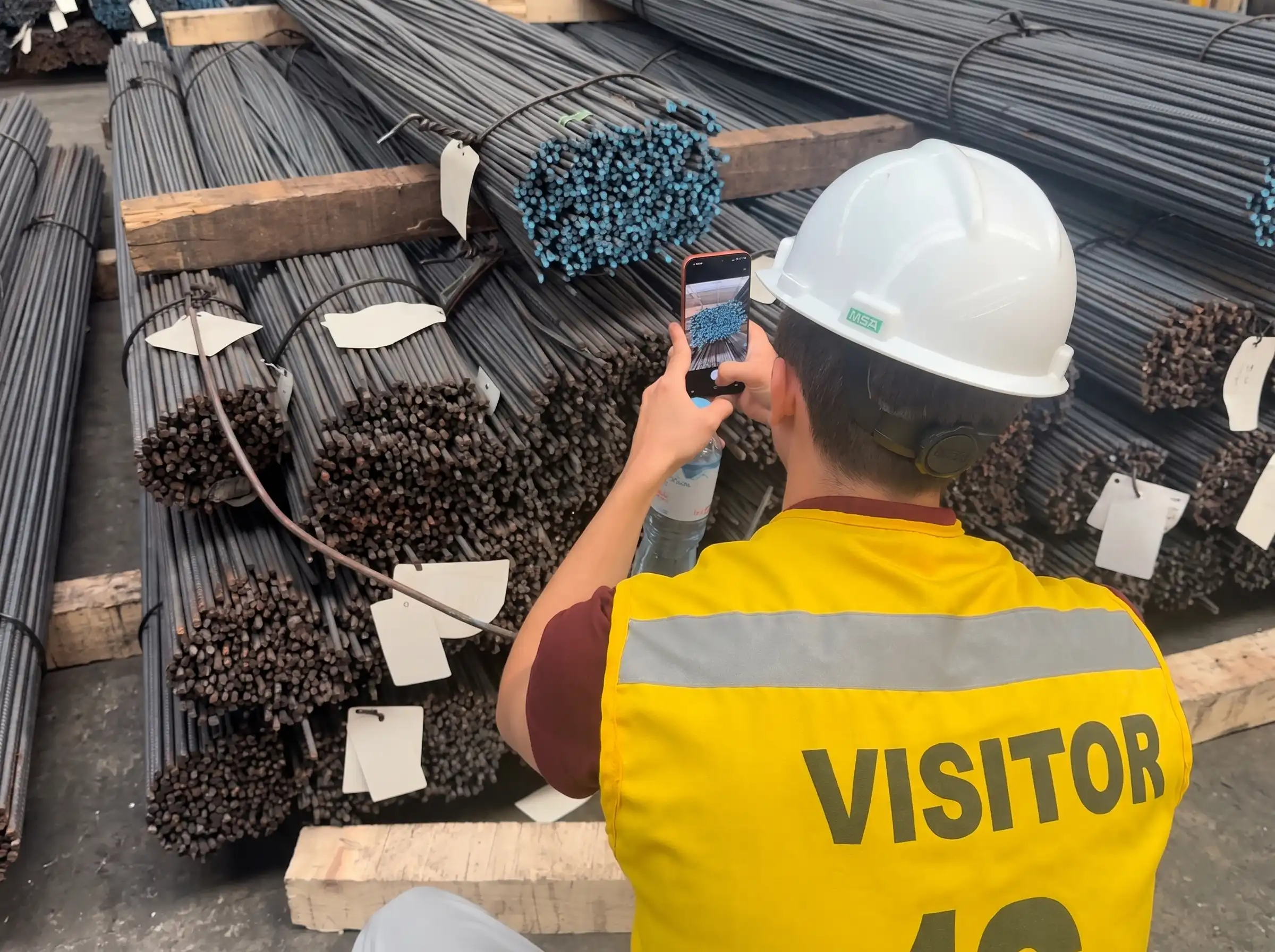 Operador logístico utilizando inteligencia artificial en su smartphone para contar varillas de acero en un almacén en Perú